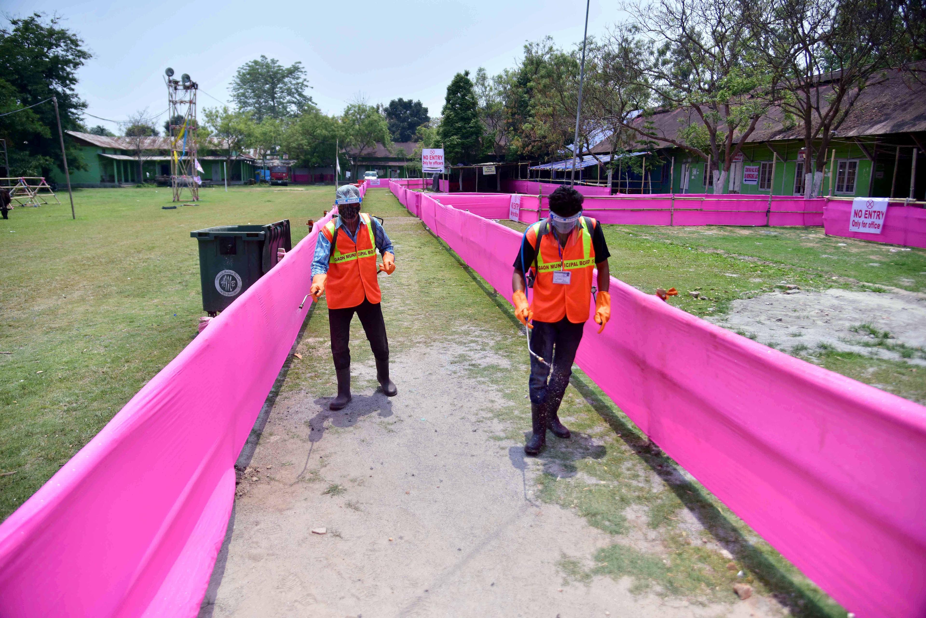 Workers spray disinfectant to sanitize inside the campus of a counting hall in Nagaon district.  (ANI Photo)