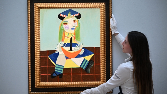 An employee works poses with an artwork entitled 'Fillette au bateau (Maya)' by Pablo Picasso, during a photo call at Sotheby's auction house in central London on February 22, 2023. - The painting is expected to realise in the region of USD 15-22 million dollars (EUR 14-20 million euros, GBP 12-18 million pounds) at auction in March. (Photo by JUSTIN TALLIS)(AFP) An employee works poses with an artwork entitled 'Fillette au bateau (Maya)' by Pablo Picasso, during a photo call at Sotheby's auction house in central London on February 22, 2023. - The painting is expected to realise in the region of USD 15-22 million dollars (EUR 14-20 million euros, GBP 12-18 million pounds) at auction in March. (Photo by JUSTIN TALLIS)(AFP)
