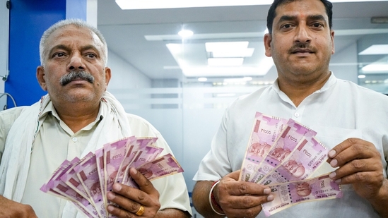 People show <span class='webrupee'>₹</span>2000 currency notes as they wait to deposit at a bank in New Delhi, Tuesday, May 23, 2023. (PTI)