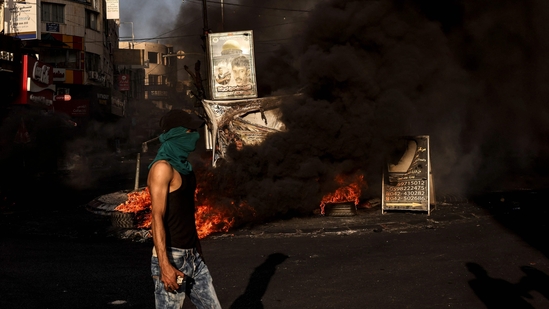 A masked man walks near a fire during clashes with the Israeli army in the occupied West Bank city of Jenin during an ongoing military operation on July 4. Israel unleashed a major raid on July 3 on Jenin refugee camp, a Palestinian militant stronghold in the Israeli-occupied West Bank, killing at least 10 Palestinians in clashes with gunmen, Reuters reported.&nbsp;(Ronaldo Schemidt / AFP)