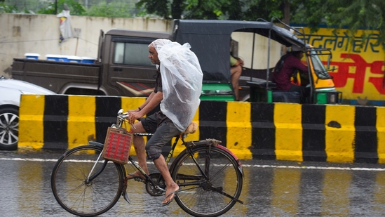A commuter on a bicycle was seen using a polythene cover to avoid getting drenched during the rain on Friday morning in Gurugram.(Parveen Kumar/HT Photo)