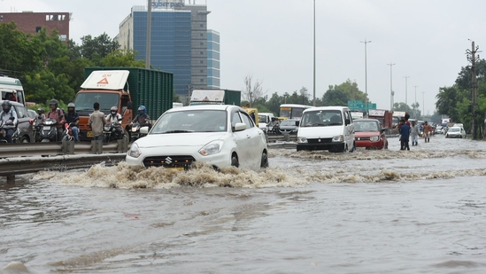 Visuals show commuters struggling through flooded areas as they travel for work or school, particularly in Baprola. Waterlogging has also affected the Delhi-Jaipur Expressway near Narsinghpur, as well as Sohna Road, Golf Course Extension Road, Basai, Hero Honda Chowk, Southern Peripheral Road (SPR), and Subhash Chowk.(Parveen Kumar/HT Photo)