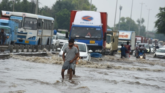 Vehicles and commuters are struggling to navigate through knee-deep water on NH-48 near Narsinghpur Village in Gurugram.(Parveen Kumar/HT Photo)